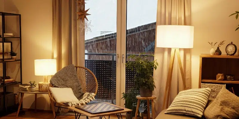 Modern bedroom with balcony glass doors, relaxing lounge chair, warm bedside lamps, and a small side table styled as part of interiors by Olangana Design’s in Bangalore.