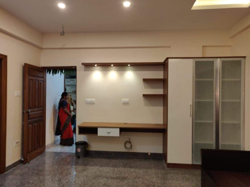 Modern living room interior design with custom TV unit, integrated storage, and display cabinets by Olangana Design in Bangalore, featuring sleek wood and white finishes, ambient lighting, and elegant granite flooring.