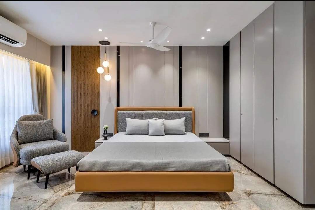 Modern bedroom interior design by Olangana Design in Bangalore featuring a grey bed, textured armchair, wooden accent wall, and sleek wardrobes.