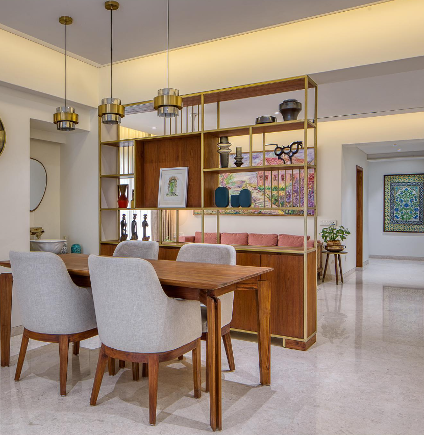 Elegant dining interior design by Olangana Design in Bangalore featuring a wooden dining table, light grey upholstered chairs, and a stylish brass and wood shelving unit with modern decor.