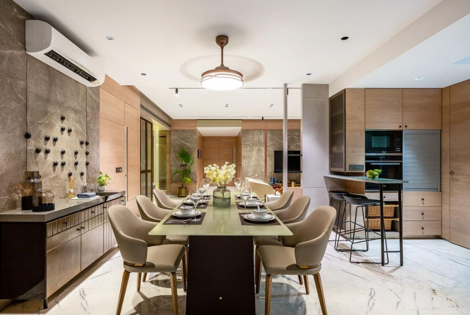 Modern dining room and kitchen interior designed by Olangana Design in Bangalore, featuring an elegant dining table, upholstered chairs, marble accent wall, and integrated kitchen cabinetry.