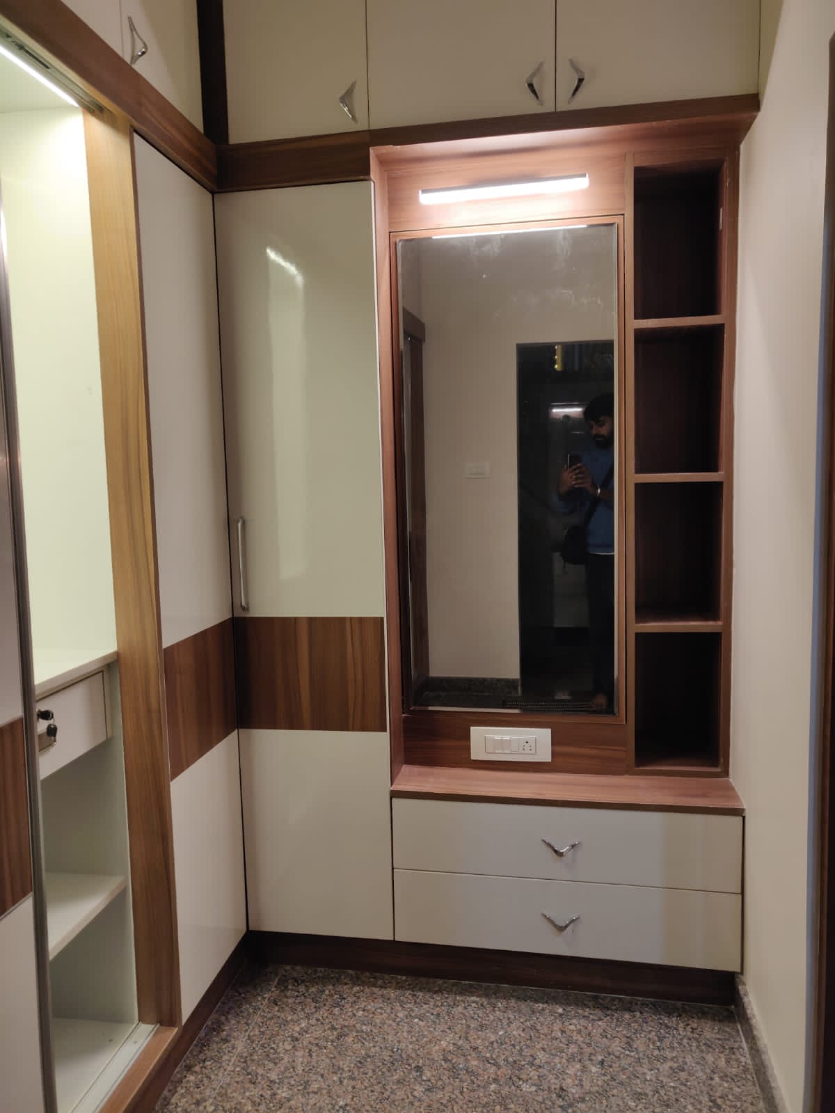 Modern wardrobe and dressing unit interior design by Olangana Design in Bangalore, featuring white and wooden finishes, ample storage, and a stylish mirror.