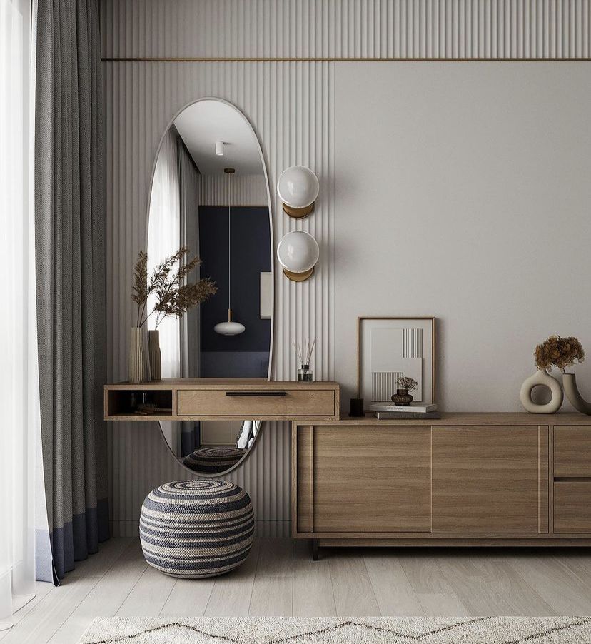 Modern minimalist interior dressing area by Olangana Design in Bangalore featuring an oval mirror, floating wooden vanity, striped pouf, and textured wall paneling.