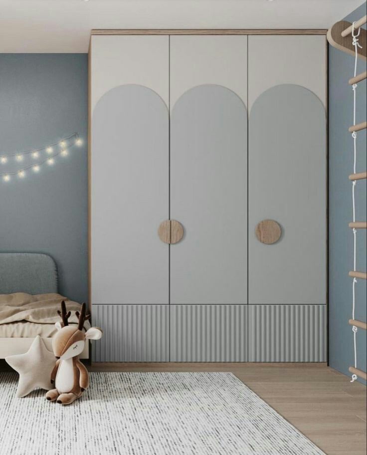 Elegant children's bedroom interior design by Olangana in Bangalore, showcasing a bespoke light grey and white wardrobe with arched details and fluted lower panels, alongside a cozy bed and playful decor.