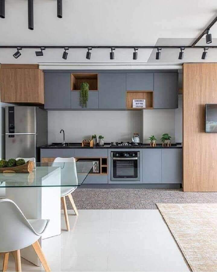 Modern open-plan kitchen and dining interior design by Olangana in Bangalore, featuring sleek grey cabinetry, warm wooden accents, a glass dining table, and contemporary track lighting.
