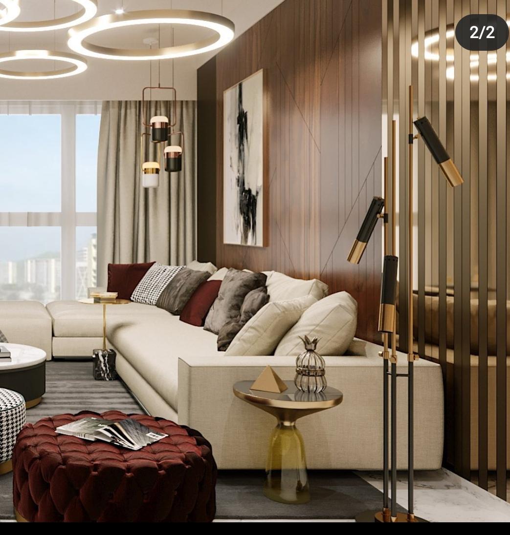 Luxurious living room interior design by Olangana in Bangalore, featuring a cream sectional sofa, rich wood paneling, modern circular and pendant lighting, and a maroon tufted ottoman.