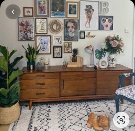 Eclectic living room interior design by Olangana in Bangalore, featuring a vibrant gallery wall above a mid-century modern wooden sideboard, adorned with plants and unique decor, set on a stylish patterned rug.