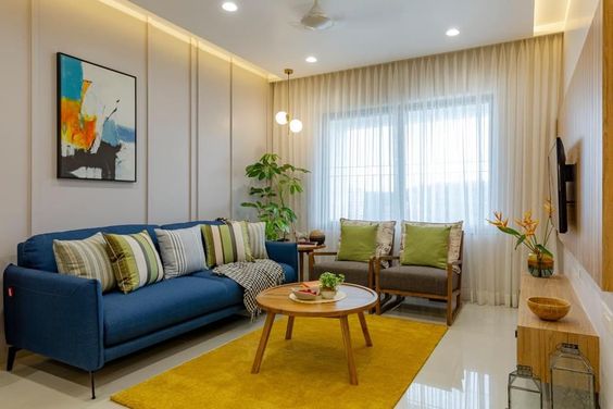 Modern living room interior design by Olangana in Bangalore, featuring a navy blue sofa, vibrant yellow rug, abstract art, and elegant wooden furniture.
