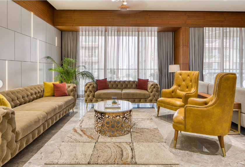 Luxurious living room interior design by Olangana in Bangalore, featuring plush tufted sofas, vibrant mustard armchairs, a geometric gold coffee table, and elegant ambient lighting.