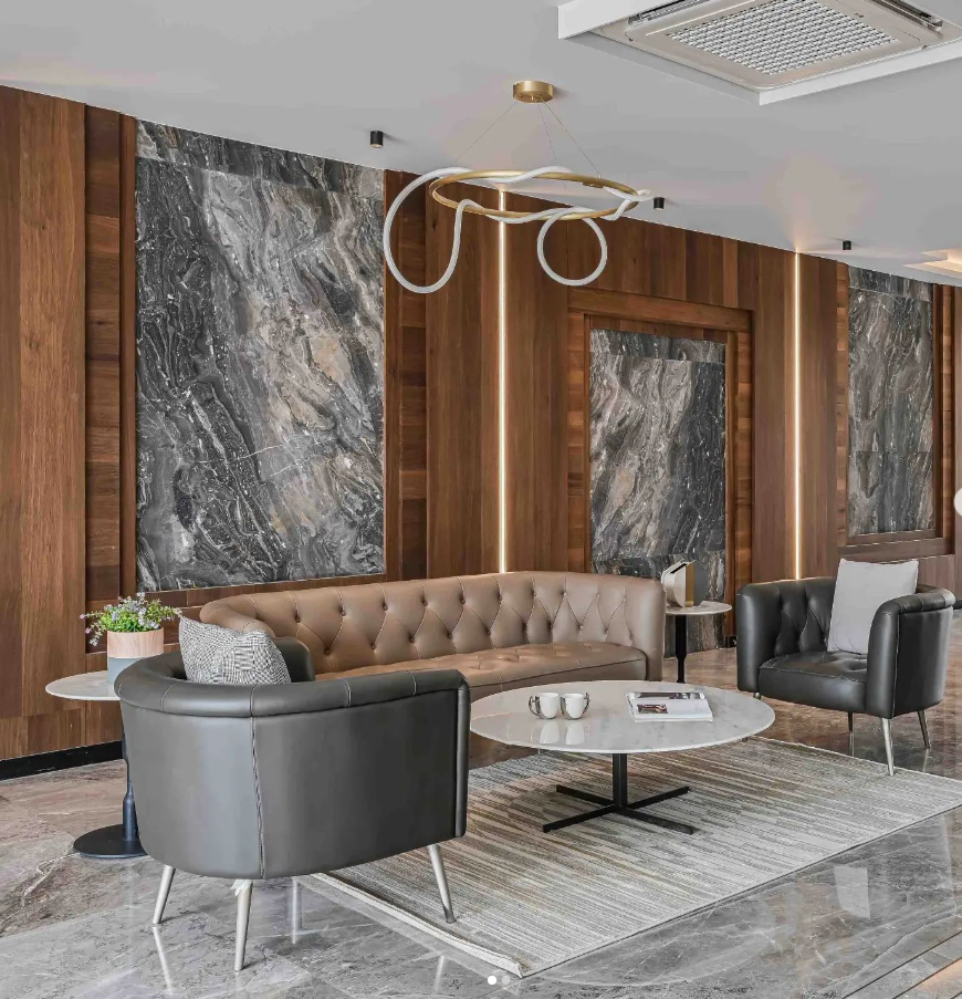 Luxurious lounge interior design by Olangana in Bangalore, showcasing a tufted sofa, dark armchairs, a marble coffee table, and a striking modern chandelier amidst wood and marble paneling.