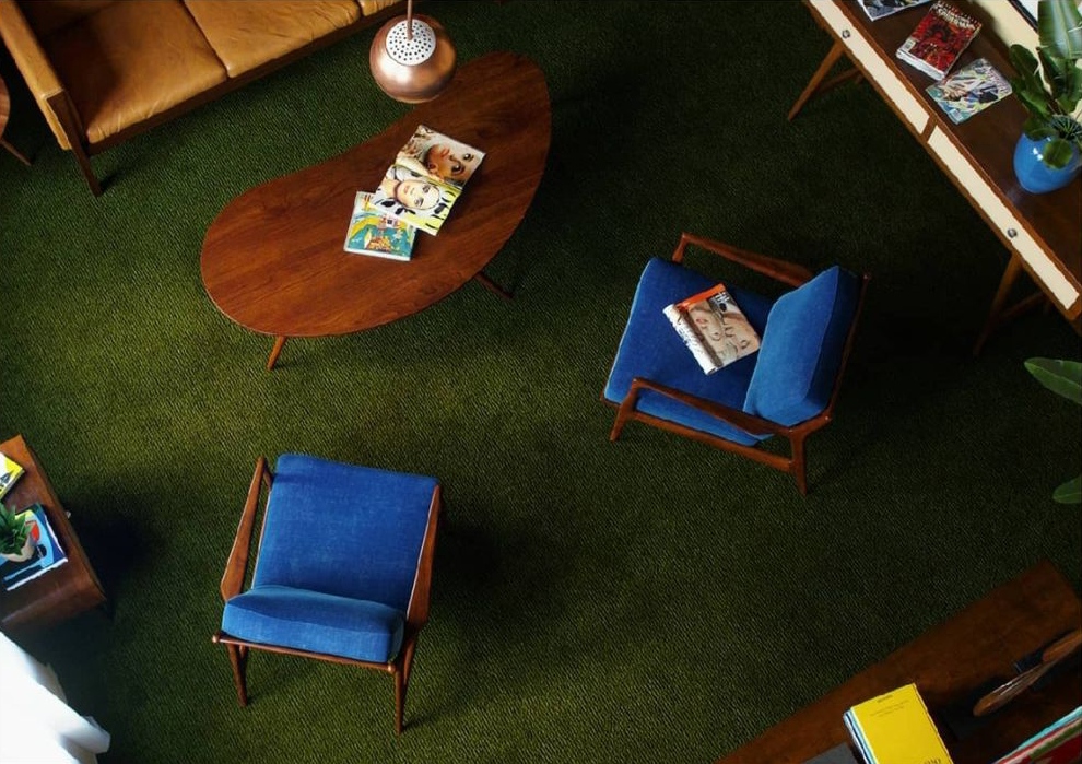 Overhead view of a sophisticated mid-century modern living room interior design by Olangana in Bangalore, featuring a vibrant olive green carpet, a stylish wooden coffee table, and elegant blue upholstered chairs.