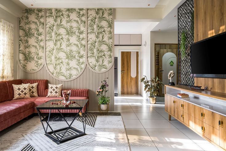 Modern living room interior design by Olangana in Bangalore, featuring a coral velvet L-shaped sofa, botanical wallpaper, and a sleek wooden TV unit with a geometric partition.