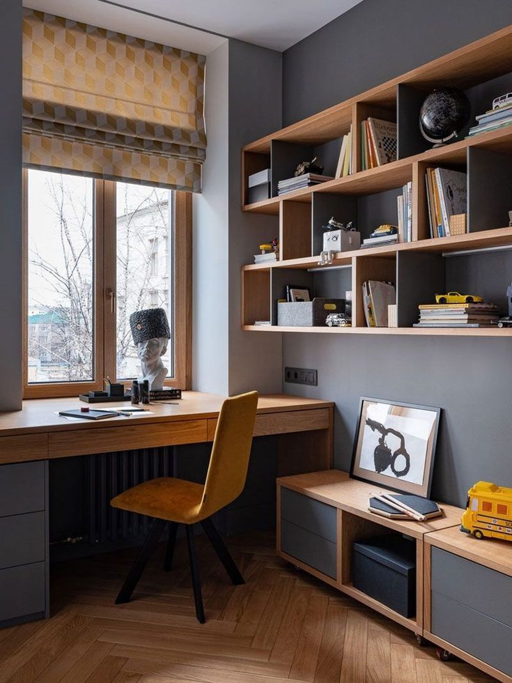 A modern and inviting home office interior design by Olangana in Bangalore, featuring a sleek natural wood desk, a vibrant mustard yellow velvet chair, custom grey and timber shelving, and elegant herringbone wood flooring, embodying functional and stylish Interior Design.