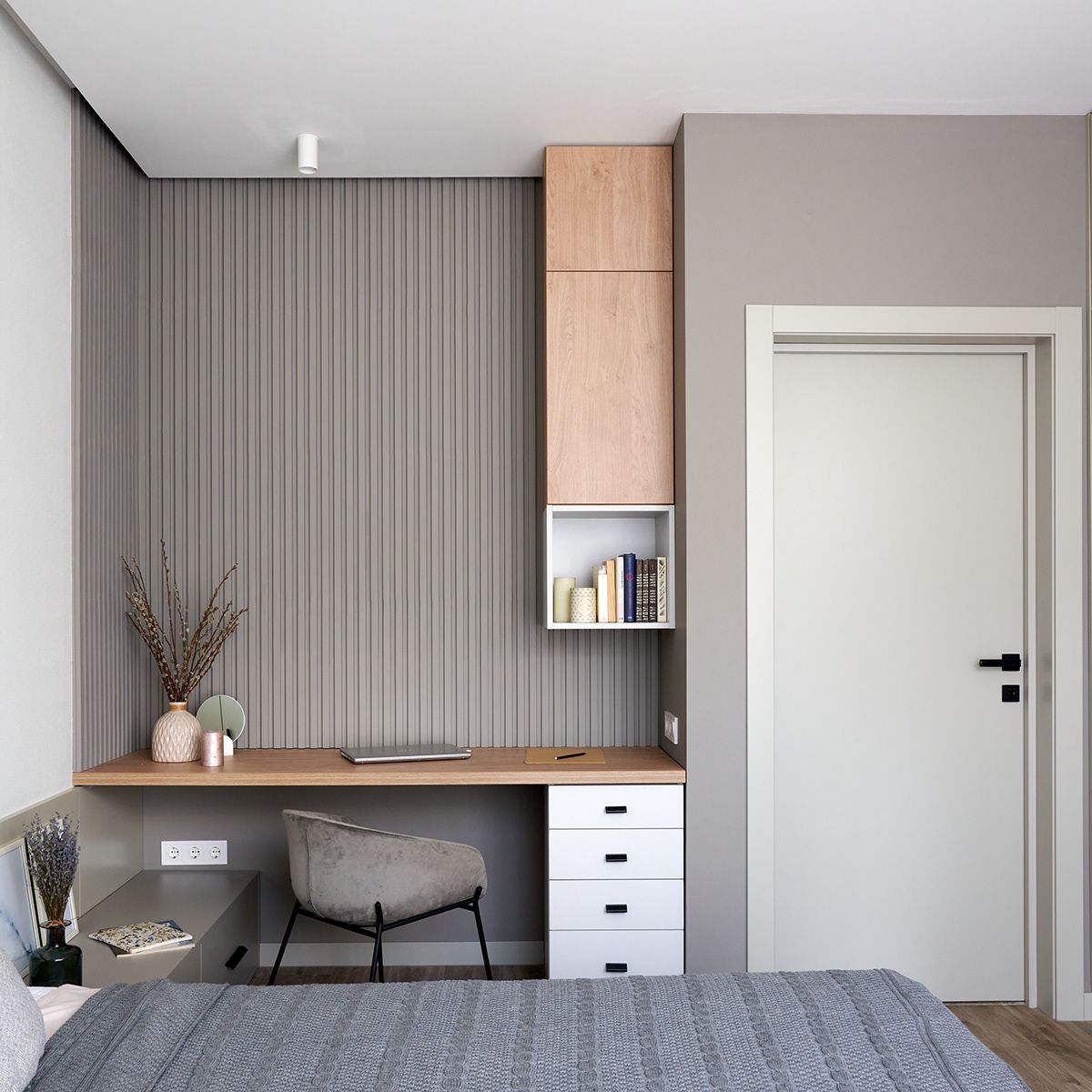 A contemporary bedroom Interior Design by Olangana, featuring a sophisticated grey slatted accent wall, a minimalist floating wooden desk, and integrated light wood storage cabinets. This modern workspace area reflects Olangana's commitment to functional elegance in Bangalore.