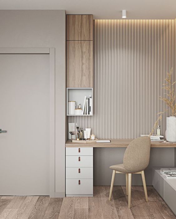 Elegant minimalist home office or vanity area designed by Olangana in Bangalore, featuring a light wood desk, white drawers with subtle leather pulls, a fluted wall panel, and warm recessed lighting, exemplifying refined Interior Design.
