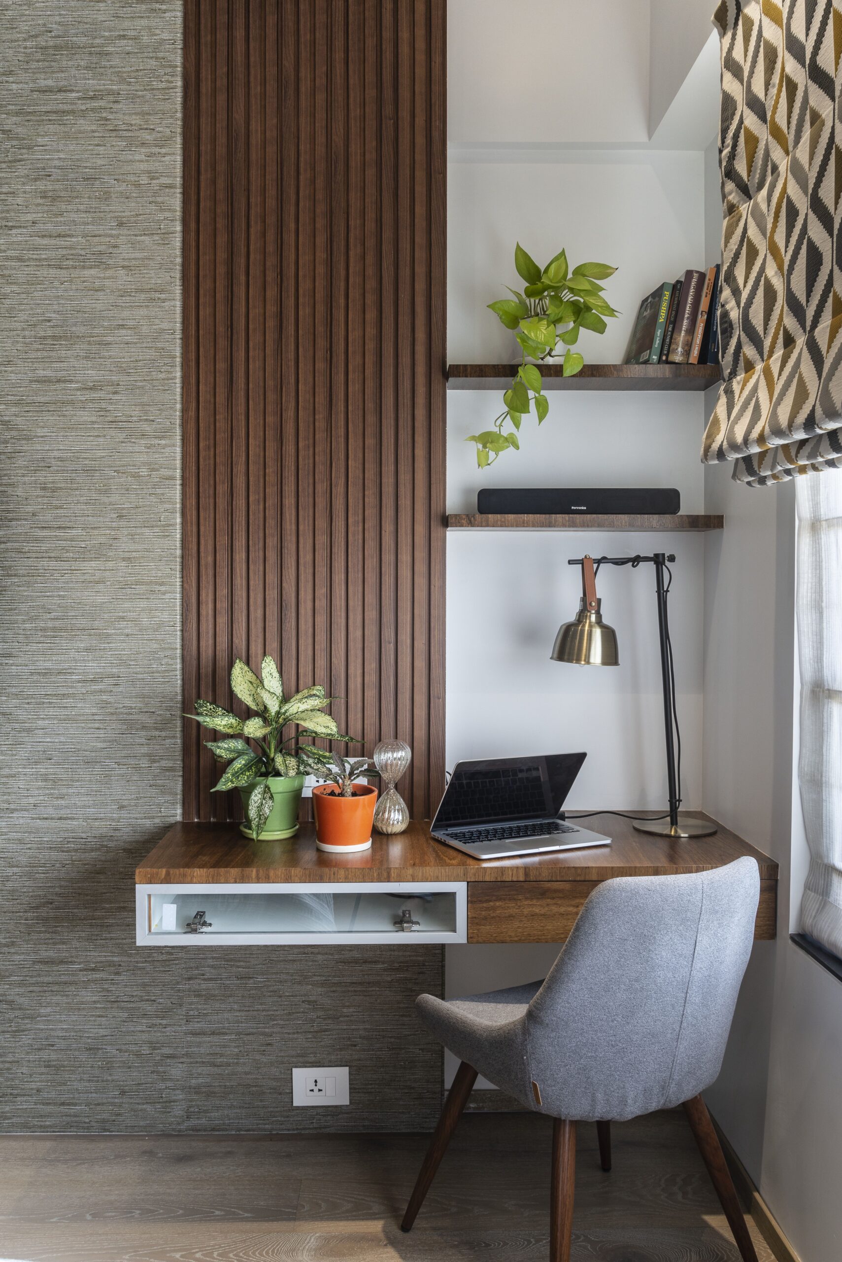 Modern home office interior design by Olangana in Bangalore, featuring a floating wooden desk, a comfortable grey chair, and natural plant decor.