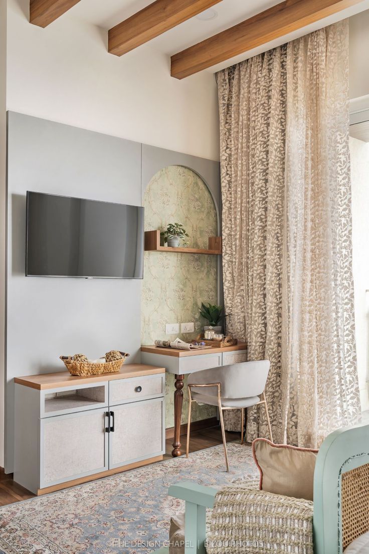 An elegant home office nook and TV unit in a contemporary Bangalore residence, featuring light grey paneling, natural wooden ceiling beams, a chic vanity desk with a gold-framed chair, and soft patterned curtains. This inviting Interior Design by Olangana expertly blends functionality with sophisticated style.