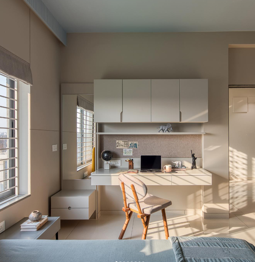 A sophisticated modern study nook and home office interior design by Olangana in Bangalore, featuring a sleek built-in desk with overhead cabinets, a comfortable wooden chair, and a warm, neutral color palette bathed in natural light, showcasing exquisite interior design for productivity.