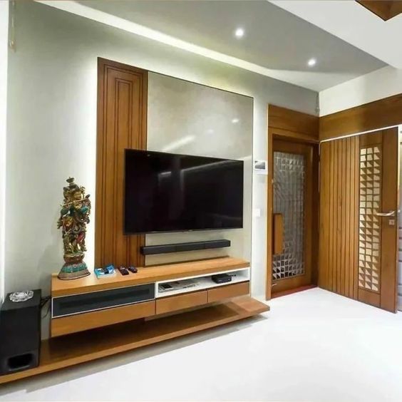 Modern Interior Design by Olangana in Bangalore, showcasing a sophisticated TV unit with elegant wooden paneling, a neutral accent wall, and ambient cove lighting. The design features a sleek floating console and a traditional decorative statue, reflecting Olangana's exquisite taste.