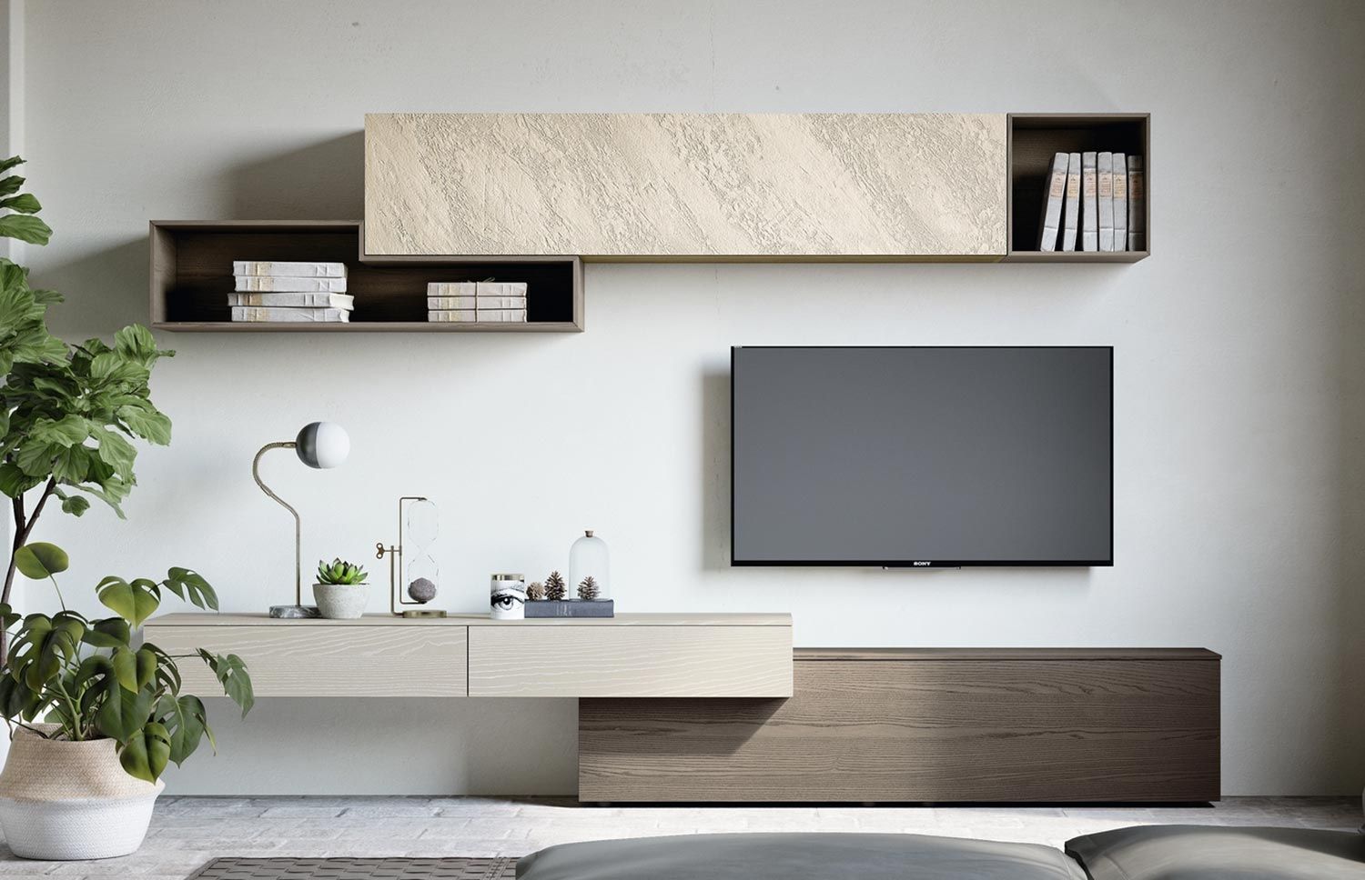 A sleek, modern living room media unit designed by Olangana, featuring light wood floating consoles, dark wood open shelving with books, a textured cream wall panel, and vibrant green plants, embodying contemporary Interior Design excellence in Bangalore.