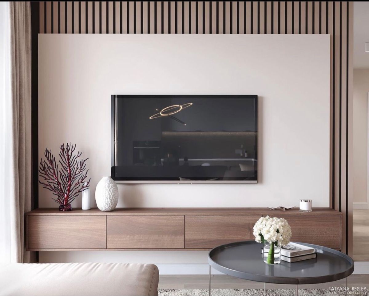Elegant living room Interior Design by Olangana in Bangalore, featuring a modern wall-mounted TV against an off-white wall with decorative vertical wooden slats, a floating walnut wood console, and minimalist decor including a vibrant red coral art piece.
