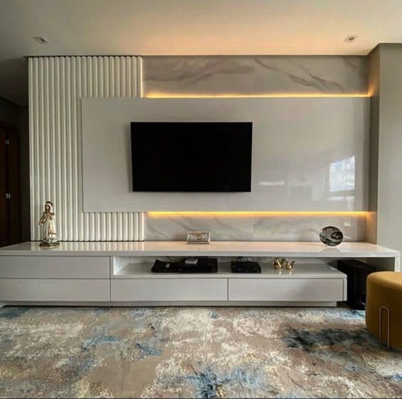 A luxurious modern living room featuring a sleek white TV unit with fluted wall panels and warm LED strip lighting illuminating elegant marble accents, expertly crafted by Olangana for exceptional Interior Design in Bangalore.