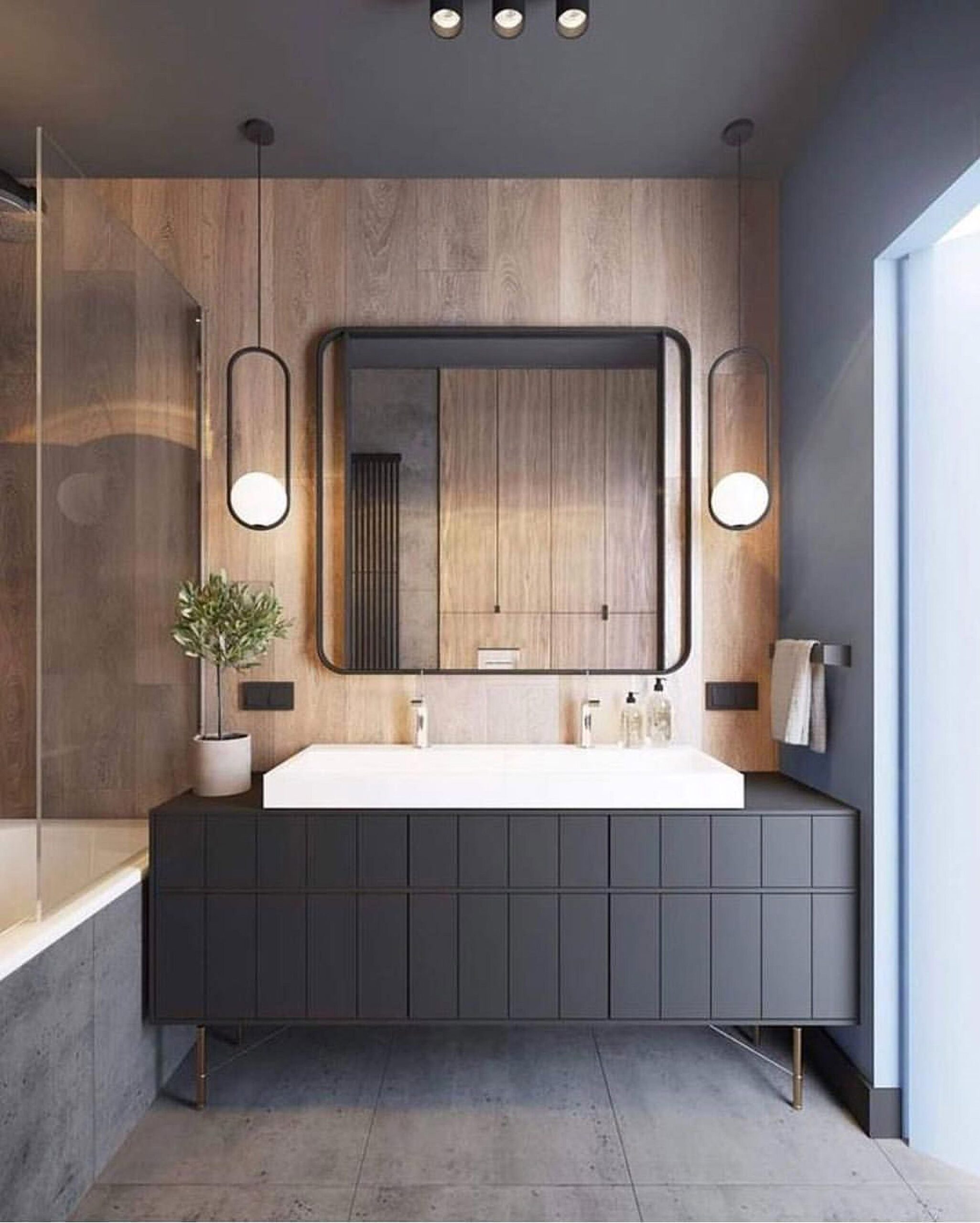 A luxurious modern bathroom interior design by Olangana in Bangalore, featuring a dark grey double vanity with a white countertop, striking wooden accent wall, minimalist rectangular mirror, and elegant pendant lighting for a sophisticated ambiance.