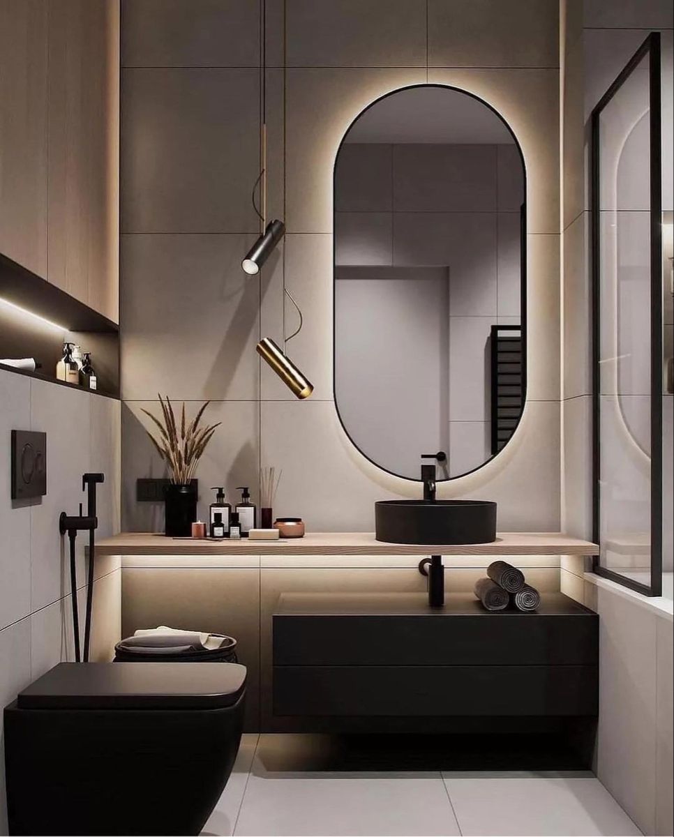 A sophisticated modern bathroom Interior Design by Olangana Design in Bangalore, featuring sleek matte black fixtures, a floating vanity with a black vessel sink, and an elegantly illuminated oval mirror. Contemporary pendant lights and warm under-shelf lighting create a luxurious ambiance, showcasing Olangana's exquisite style.