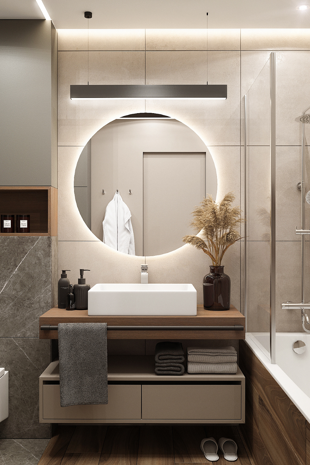 A sophisticated bathroom interior design by Olangana in Bangalore, showcasing a modern floating wooden vanity with a white rectangular basin, a prominent backlit round mirror, and elegant linear lighting. The space features a warm neutral color palette with beige tiled walls, a glass shower partition, and neatly arranged towels, epitomizing luxury Interior Design.