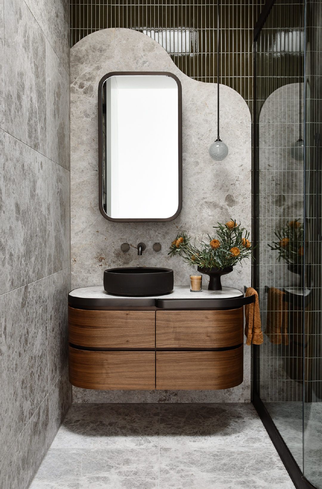 Elegant contemporary bathroom interior design by Olangana, featuring a floating dark wood vanity, a sleek black vessel sink, and a rectangular mirror against luxurious grey marble walls with textured olive green accent tiles. Ideal for modern homes in Bangalore, showcasing sophisticated Interior Design.
