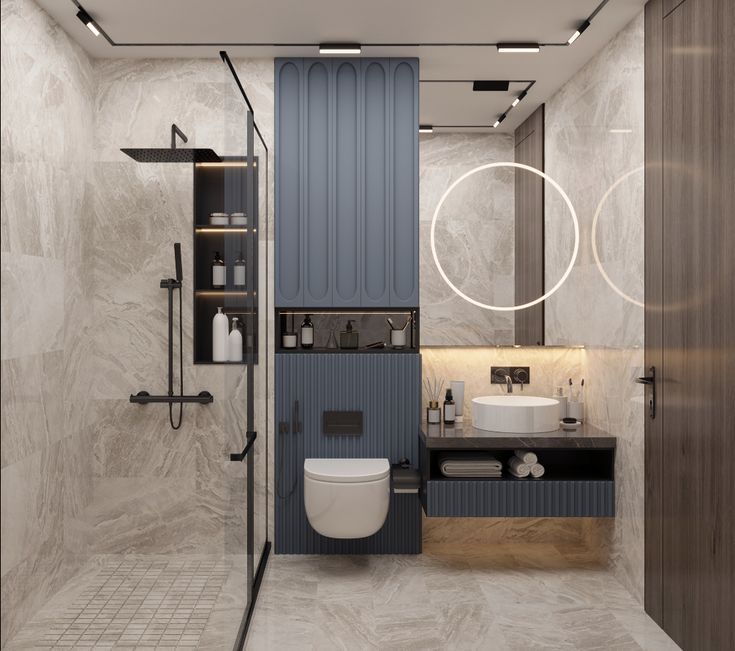 Elegant modern bathroom interior design by Olangana in Bangalore, featuring luxurious grey marble walls, sophisticated blue fluted cabinetry, a sleek walk-in shower with matte black fixtures, a wall-mounted toilet, and a contemporary vanity with a circular illuminated mirror, highlighting Olangana's premier Interior Design expertise.
