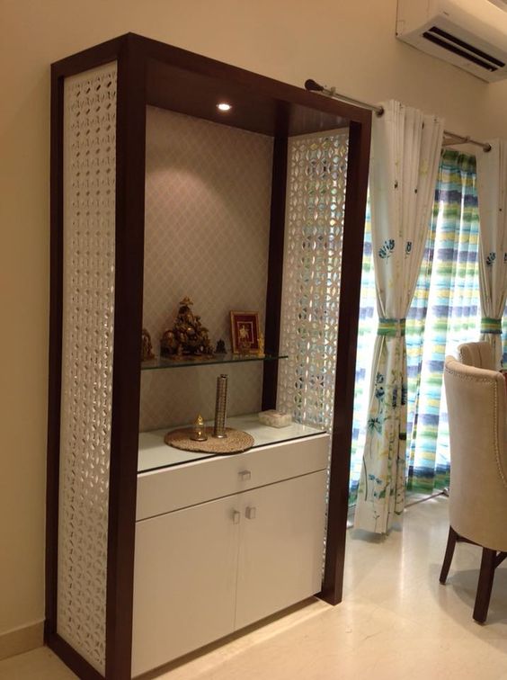 Modern pooja unit interior design by Olangana in Bangalore, featuring a dark wood frame, intricate white jali panels, a glass shelf for idols, and integrated storage.