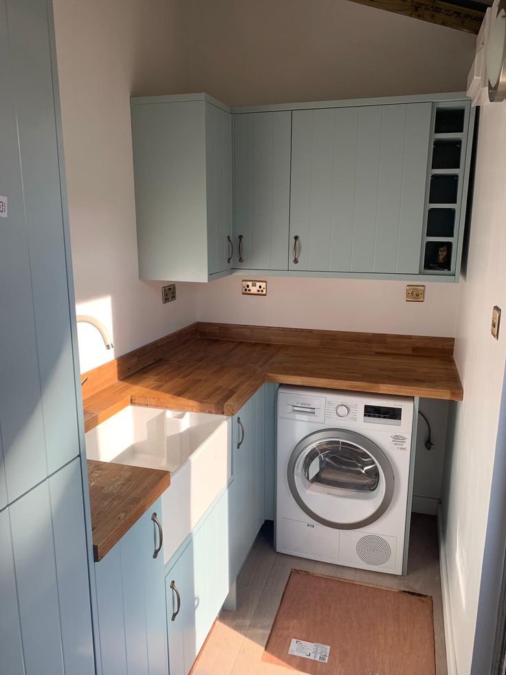 A sophisticated utility room Interior Design by Olangana, showcasing light blue shaker-style cabinetry with warm wooden countertops and a classic white farmhouse sink, expertly optimizing space in Bangalore.