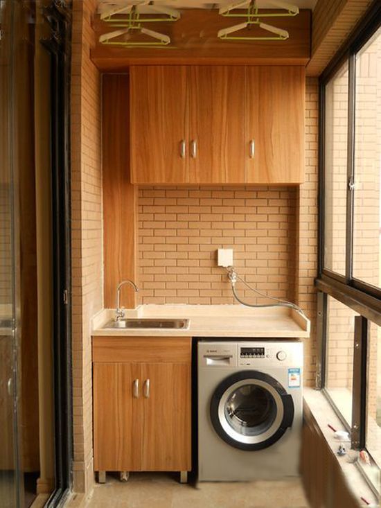 A compact and highly functional balcony laundry area showcasing light wood cabinets, a sleek stainless steel sink, and an integrated washing machine, exemplifying smart Interior Design by Olangana for homes in Bangalore.