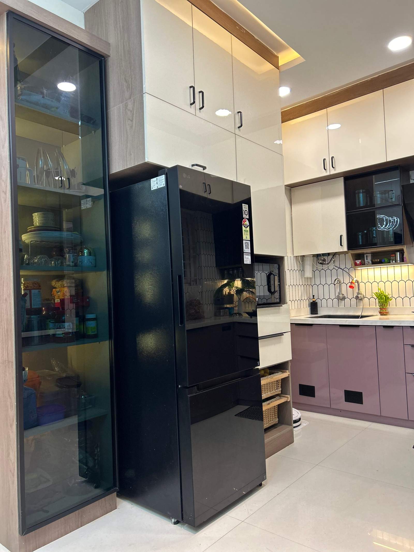 Contemporary modular kitchen with chimney, fridge placement, glass rack cabinet, and modern storage units in Bangalore home interiors.