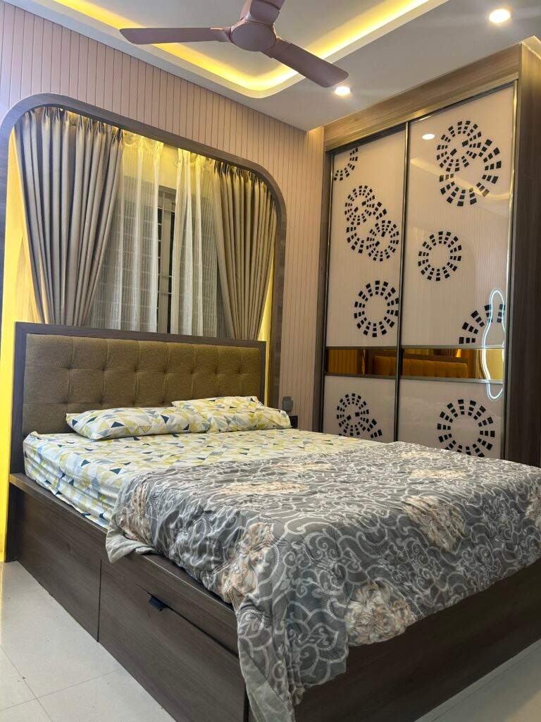 Modern master bedroom interior in a Bangalore home with warm lighting, sleek sliding wardrobe, POP ceiling design, stylish fan, well-proportioned bed, and elegant window curtains designed by Olangana Design’s.