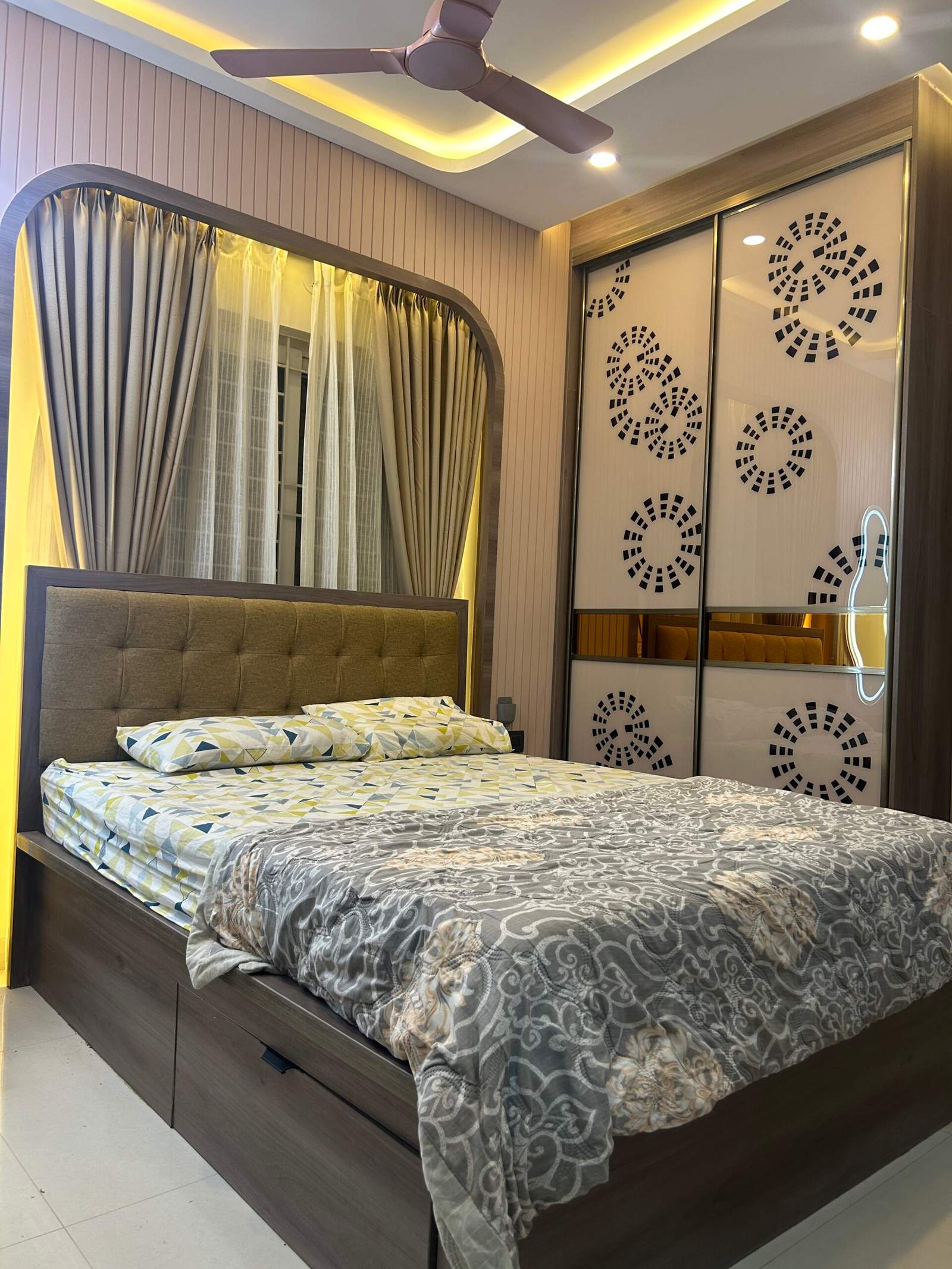 Modern master bedroom interior in a Bangalore home with warm lighting, sleek sliding wardrobe, POP ceiling design, stylish fan, well-proportioned bed, and elegant window curtains designed by Olangana Design’s.