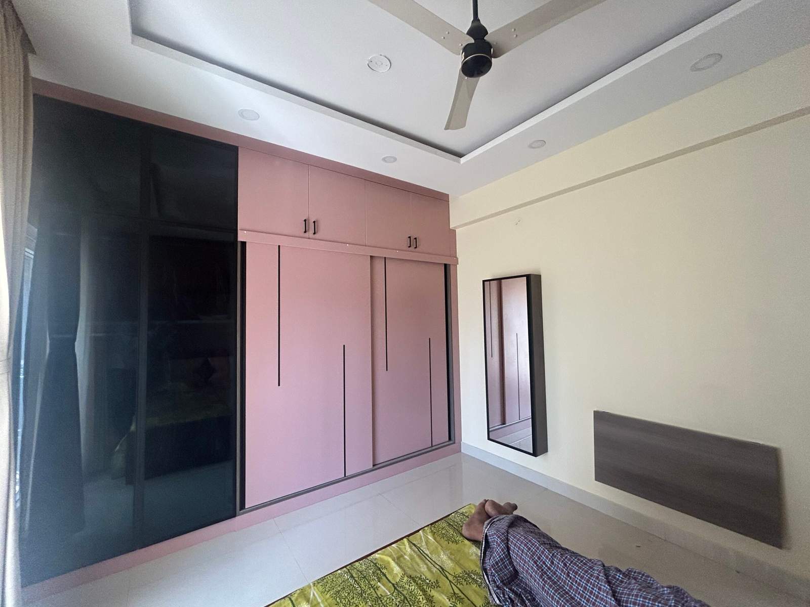 Modern master bedroom interior with pink sliding wardrobe, simple dressing mirror, and wall-mounted ironing table designed by Olangana Design’s.