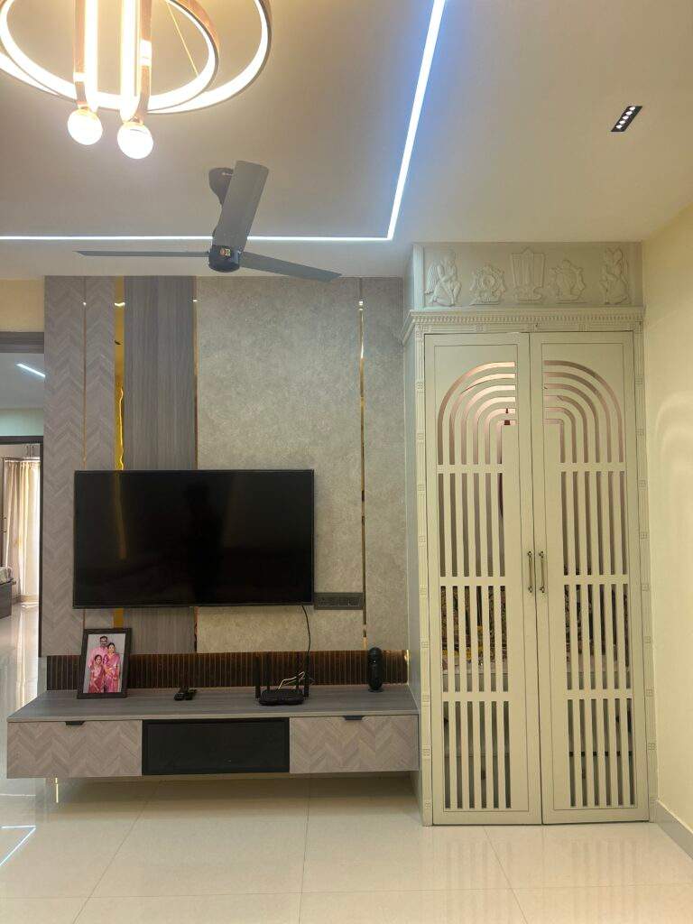Hall pooja unit with decorative doors beside TV cabinet in Bangalore home by Olangana Design’s.